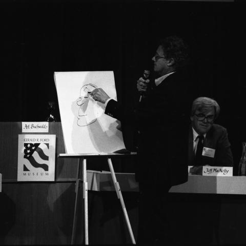 artist standing at an easel speaking into a microphone while drawing