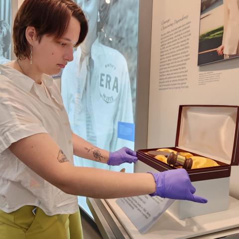 An intern, wearing gloves, adjusts a box containing a gavel. 