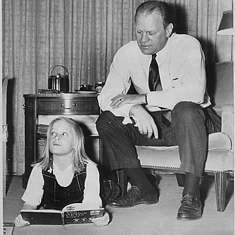 H0042-4. Gerald R. Ford watches as his daughter Susan lies on the floor and reads from "Ten Apples Up On Top" in the living room of the Ford residence at 514 Crown View Drive, Alexandria, VA. 1964.