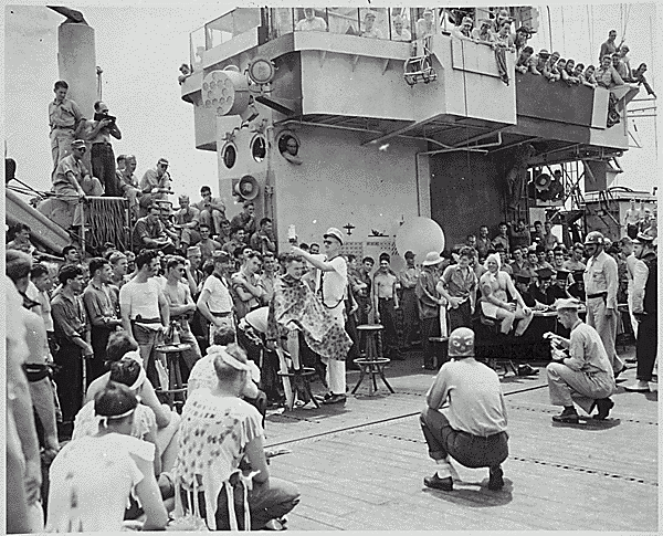 H0061-1. Gerald R. Ford, Jr. and members of the crew of the USS MONTEREY watch the festivities as the ship crosses the equator and other crew members pay homage to King Neptune. Gerald Ford is seated at top, to right of the superstructure, right hand on chin and left hand across his knee. 1944.
