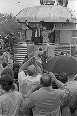 A9804-26A. President and Mrs. Ford wave from the rear of the train during their primary campaign whistle-stop tour of Michigan.  Durand, Michigan.  May 15, 1976.