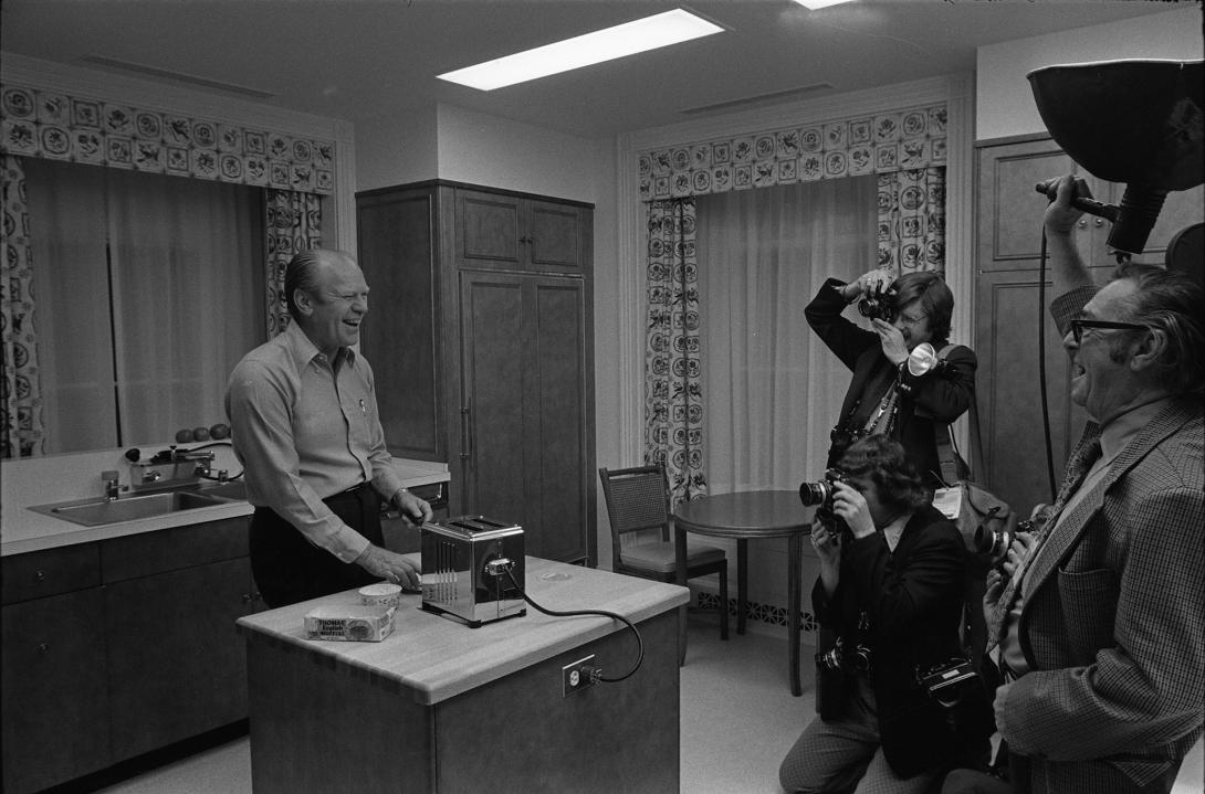 A0532-15. President Ford shows off his English Muffin toasting technique for the press in the White House residence kitchen. September 5, 1974.