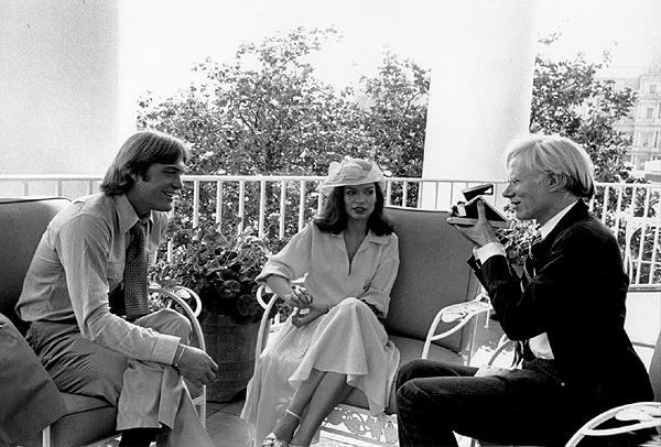 A5345-30. Andy Warhol takes a photograph of Jack Ford as Bianca Jagger looks on. The three met on the balcony off the White House residence. July 2, 1975.