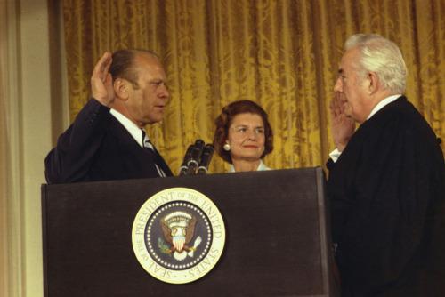 Gerald R. Ford stands behind podium with hand raised as he is sworn in as the 38th President of the United States