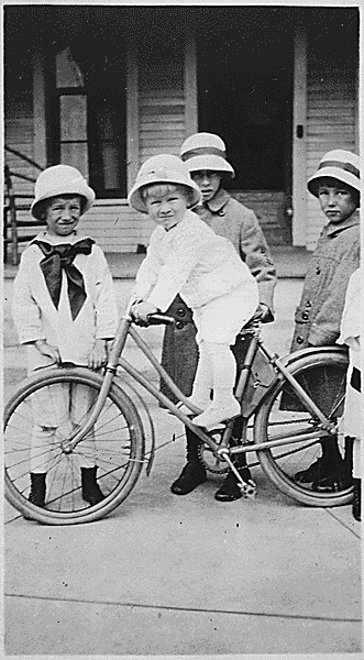 H0021-1. Gerald R. Ford, Jr. (then known as Leslie Lynch King, Jr.) seated on a bicycle, poses with his cousin Gardner James and two unidentified girls.